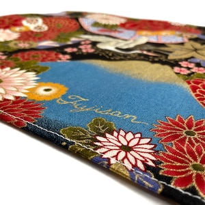 May include: Close-up of a fabric with a Japanese floral design. The fabric features a blue background with the word "Fujisan" in gold script. Red, white, and yellow flowers are scattered across the fabric.