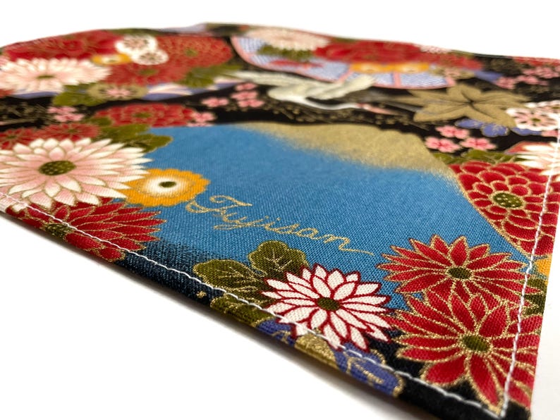 May include: Close-up of a fabric with a Japanese floral design. The fabric features a blue background with the word "Fujisan" in gold script. Red, white, and yellow flowers are scattered across the fabric.