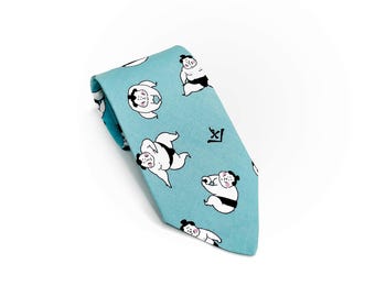 May include: A light blue necktie featuring a repeating pattern of cartoon sumo wrestlers in various poses. The tie has a simple design with a small Japanese character near the knot. The background is white.