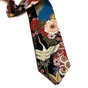 May include: A necktie featuring a black background with a vibrant pattern of white cranes, red and white chrysanthemums, and gold accents. The design includes a blue section at the top and intricate floral motifs throughout the fabric surface.