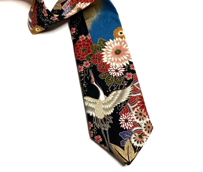 May include: A necktie featuring a black background with a vibrant pattern of white cranes, red and white chrysanthemums, and gold accents. The design includes a blue section at the top and intricate floral motifs throughout the fabric surface.