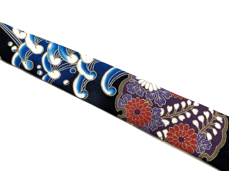 Peut inclure: Une cravate bleue et noire avec un motif floral blanc et or. La cravate pr&eacute;sente un motif de vagues et de fleurs stylis&eacute;es.