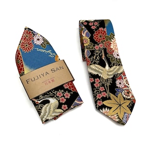 May include: A Japanese-style necktie and pocket square set. The tie and pocket square feature a black background with a crane, red and white flowers, and gold accents. The pocket square is in a box with the text "FUJIYA SAN" and "MADE IN JAPAN".