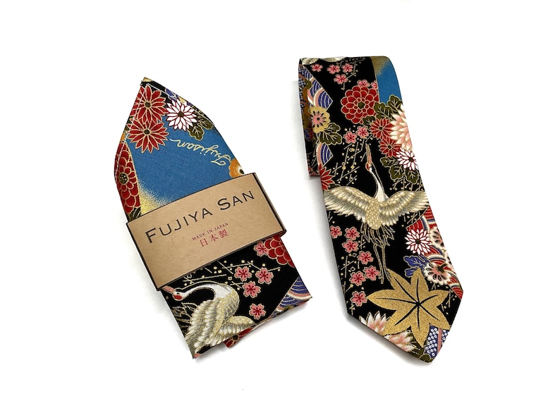 May include: A Japanese-style necktie and pocket square set. The tie and pocket square feature a black background with a crane, red and white flowers, and gold accents. The pocket square is in a box with the text "FUJIYA SAN" and "MADE IN JAPAN".