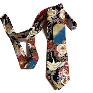 May include: A black necktie featuring a vibrant pattern of white cranes, red and white chrysanthemums, gold maple leaves, and blue geometric accents. The fabric displays a detailed floral and bird motif across the entire length of the tie.