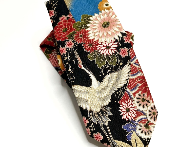 May include: A necktie featuring a black background with a detailed pattern of white cranes, red and pink chrysanthemums, and gold accents. The fabric displays a complex floral and bird motif with blue and green highlights throughout the design.
