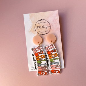 May include: A pair of colourful acrylic earrings with the text "HEALING is not linear" in a retro font. The earrings are attached to peach-coloured round dangles.