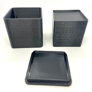 May include: Two black square boxes with a black square lid. The boxes are made of a textured plastic material.