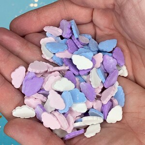 May include: A handful of pastel-coloured cloud sprinkles. The sprinkles are in shades of pink, purple, blue, and white.