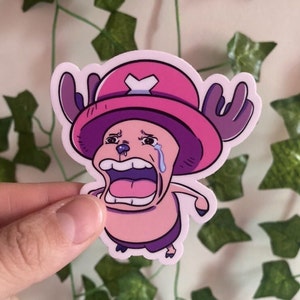 以下が含まれることがあります： ピンクとパープルの漫画のキャラクターで、角と白いXの付いたピンクの帽子をかぶっています。キャラクターは口を大きく開けて泣いています。キャラクターはステッカーです。