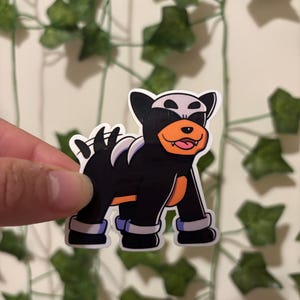 May include: A sticker featuring a cartoon dog with black fur, white markings, and orange accents. The dog has a happy expression with its tongue sticking out. The sticker is held against a background of faux ivy.