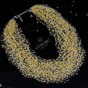 Könnte beinhalten: Eine goldene Perlenkette mit einem zarten Kettenverschluss. Die Kette besteht aus kleinen, runden Perlen, die in einem lockeren, fließenden Stil zusammengefügt sind. Die Perlen sind hellgoldfarben und haben einen dezenten Schimmer.