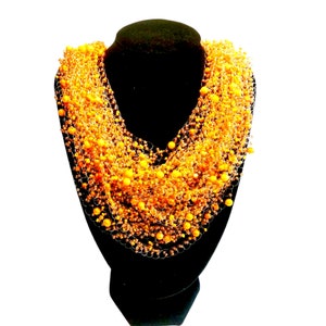 Könnte beinhalten: Eine lange, mehrreihige Halskette aus kleinen, goldenen Perlen. Die Halskette wird auf einer schwarzen Mannequin-Büste präsentiert.