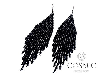 May include: A pair of long black beaded earrings with a fringe design. The earrings are made of small black beads and have a simple, elegant look.