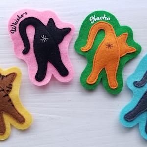 May include: Four felt cat tail toys with different colors and names. The cat tails are brown, orange, black, and blue. The names are Tiger, Nacho, Whiskers, and Blue.