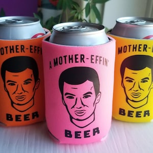 May include: Three beer can coolers in orange, pink, and yellow. Each cooler has a black illustration of a man's face and the words "A MOTHER-EFFIN' BEER". The cans are silver.