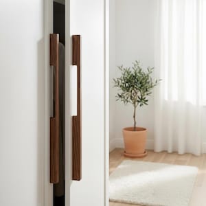 May include: Two vertical, rectangular dark brown wooden cabinet handles mounted on white doors. The handles feature a smooth, straight-edged design with a visible wood grain texture, providing a contrast against the flat, matte white surface of the doors.