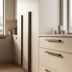 May include: A kitchen featuring floor-to-ceiling cabinetry in a matte beige finish with long, vertical dark wood handles. The lower section includes a stack of three drawers with horizontal dark wood pulls, complemented by light wood flooring.