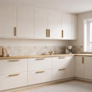 May include: A kitchen featuring off-white cabinets with light wood handles, a light wood countertop, and a tiled backsplash. The layout includes upper and lower cabinetry, a white coffee maker, and a window with a small potted plant on the sill.