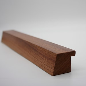 May include: A dark brown wooden cabinet pull with a rectangular shape and a cut-out on the top.