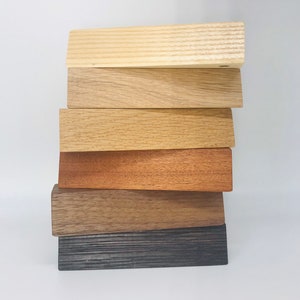 Può includere: Una pila di sei assi di legno in varie tonalità di marrone, dal chiaro al scuro. Le assi sono disposte dalla più chiara alla più scura, con l'asse più chiara in cima e l'asse più scura in fondo.