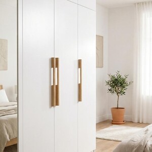 May include: A floor-to-ceiling white wardrobe featuring a mirrored door on the far left and four vertical light wood handles centered on the cabinet doors. The wardrobe has a smooth, matte finish and spans the height of the room, providing storage.