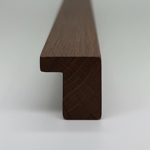 Puede incluir: Primer plano de un marco de madera marrón oscuro con un perfil cuadrado. El marco tiene un diseño escalonado en un extremo y la veta de la madera es visible. El marco es probablemente para una obra de arte o un espejo.