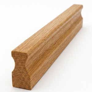 May include: A linear piece of light brown oak wood with a distinct grain pattern. The object features a rectangular base that transitions into a concave middle section, topped with a wider, flat surface, creating a profile resembling a rail.