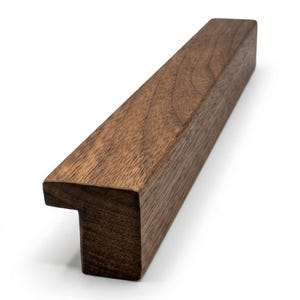 May include: A rectangular wooden drawer pull with a T-shaped end. The pull is made of dark brown wood and has a smooth, polished finish. The design is modern and minimalist, suitable for various furniture styles.