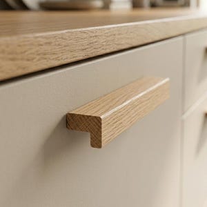 May include: A light beige cabinet door featuring a horizontal, L-shaped wooden handle with a visible natural oak grain. The cabinet is topped with a matching light oak wood countertop, creating a clean and cohesive look for the kitchen cabinetry.