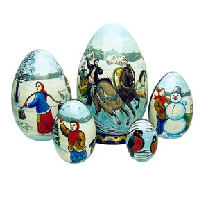 Peut inclure: Un ensemble de cinq poupées russes gigognes, ou poupées matriochkas, peintes avec des scènes d'hiver. La plus grande poupée représente un traîneau tiré par des chevaux avec des personnes qui y montent. Les autres poupées représentent un bonhomme de neige, une femme portant un seau, une fille tenant un arbre et deux oiseaux sur une branche.