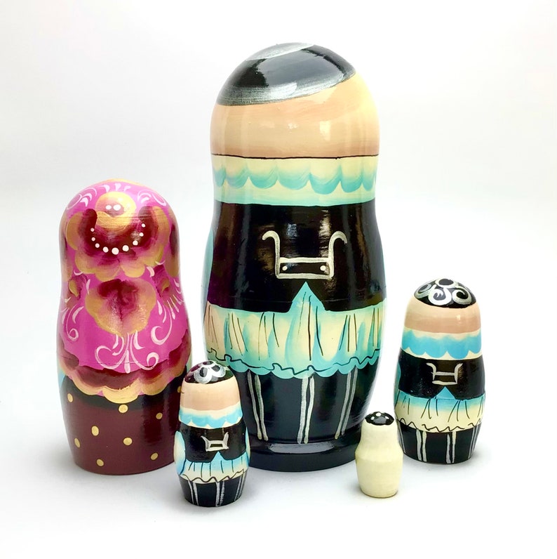 以下が含まれることがあります： 6体のロシアのマトリョーシカ人形のセット。人形は手描きで、ピンク、黒、青、ベージュの色合いで詳細なデザインが施されています。一番大きい人形は約15cmです。一番小さい人形は無塗装の木製です。
