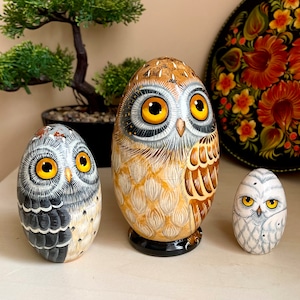 Peut inclure: Trois figurines de hiboux en bois peintes à la main. Le plus grand hibou est brun et blanc avec des yeux jaunes. Le hibou de taille moyenne est gris et blanc avec des yeux jaunes. Le plus petit hibou est blanc avec des yeux noirs.