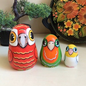 Peut inclure: Trois poup&eacute;es russes en bois peintes &agrave; la main en forme d'oiseaux. La plus grande poup&eacute;e est rouge avec des accents orange et jaunes, la poup&eacute;e du milieu est verte avec des accents orange et jaunes, et la plus petite poup&eacute;e est jaune avec des accents blancs.