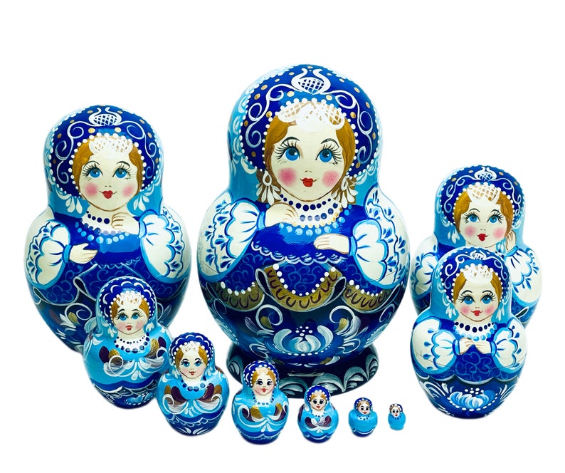 Puede incluir: Un conjunto de 10 mu&ntilde;ecas rusas de anidaci&oacute;n, o mu&ntilde;ecas matrioska, azules y blancas, con intrincados dise&ntilde;os florales y detalles dorados. La mu&ntilde;eca m&aacute;s grande mide aproximadamente 25 cm de alto y la m&aacute;s peque&ntilde;a aproximadamente 2,5 cm.