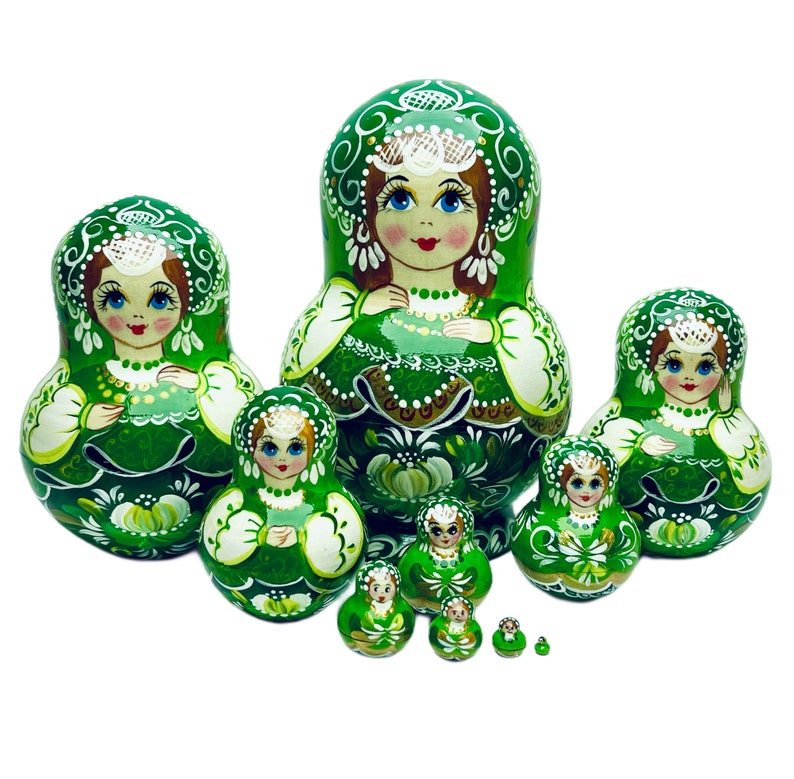 Puede incluir: Un conjunto de 8 mu&ntilde;ecas rusas de anidaci&oacute;n verdes y blancas. La mu&ntilde;eca m&aacute;s grande mide aproximadamente 15 cm de alto y la m&aacute;s peque&ntilde;a aproximadamente 2,5 cm. Cada mu&ntilde;eca est&aacute; pintada con un dise&ntilde;o floral y la cara de una mujer.
