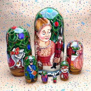 Può includere: Un set di sei bambole russe annidate dipinte a mano, o bambole matrioska, che rappresentano una scena del ballet Lo Schiaccianoci. La bambola più grande mostra una giovane ragazza con un vestito rosa in piedi accanto a un soldato Schiaccianoci. Le altre bambole rappresentano un albero di Natale, un topo, un soldato e una coppia che balla.