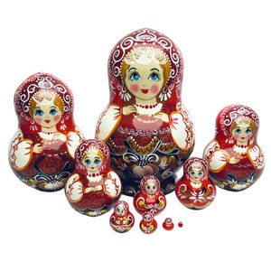 Puede incluir: Un conjunto de ocho mu&ntilde;ecas rusas de anidaci&oacute;n, tambi&eacute;n conocidas como mu&ntilde;ecas matryoshka, de color rojo y blanco. Las mu&ntilde;ecas est&aacute;n pintadas con dise&ntilde;os florales tradicionales y tienen caras sonrientes. La mu&ntilde;eca m&aacute;s grande mide aproximadamente 25 cm de alto y la m&aacute;s peque&ntilde;a aproximadamente 2,5 cm.