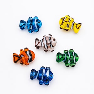 May include: Six glass fish figurines in various colours. The fish are blue, yellow, orange, green, and brown, with white stripes. Each fish has a unique design and shape, suitable for decorative purposes.