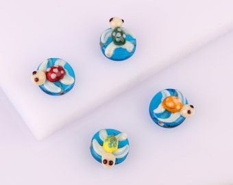 May include: Four glass turtle beads with blue, green, yellow, and red accents. The turtles are on a white background.