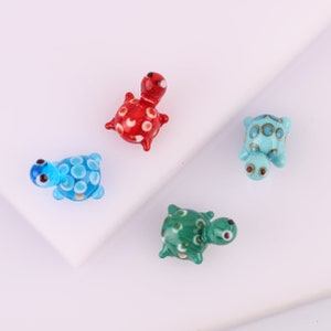 May include: Four glass turtle figurines with different coloured shells and spots. The turtles are red, blue, green, and blue with white spots.