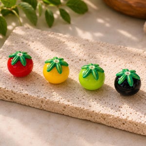Peut inclure: Quatre perles sphériques en forme de petits fruits, chacune surmontée d'une tige verte. Les perles sont respectivement de couleur rouge, jaune, vert clair et noire. Chaque perle présente un petit trou au centre de la tige pour l'enfilage.
