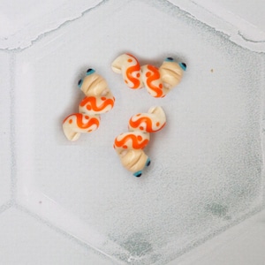 May include: Three white and orange plastic hair clips with blue eyes. The clips are shaped like a spiral.