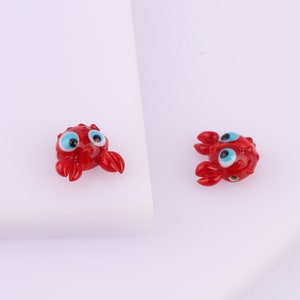 May include: Two red glass crab charms with blue eyes. The crabs have a textured surface and are about 1 inch in size.