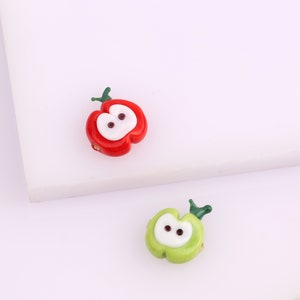 May include: Two glass apple beads, one red and one green, with white centers and black eyes. The beads are perfect for jewelry making or crafting.