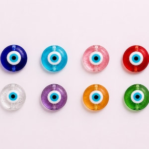 May include: Eight colorful glass evil eye beads. The beads are round with a blue, white, and black eye design. Colors include blue, turquoise, pink, red, clear, purple, orange, and green. The beads are arranged on a light pink background.