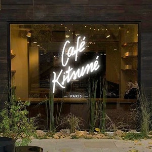Könnte beinhalten: Ein Ladenlokal mit einem Neon-Schild, auf dem "Café Kitsuné - Paris" steht.