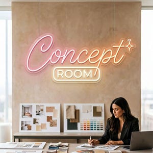 May include: A neon sign with the text "Concept Room" in pink and orange, with a white outline. The sign is 42 inches in length and hangs above a desk where a person is working. The sign is a color-changing upgrade.