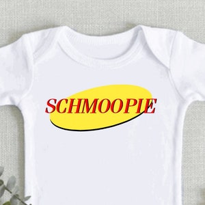 May include: White baby onesie with a yellow oval and the word "Schmoopie" in red letters.