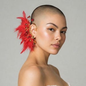 May include: An ornate ear cuff with a red feather and bead design. The gold-coloured metal ear cuff curves around the ear, embellished with red feathers and sparkling red beads, creating a striking accessory.